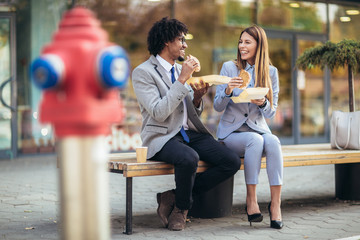 Smiling businessmen with sandwiches sitting in front of the office building - lunch break