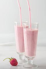 Cocktail has pink color there is in glasses with straws and marshmallows. Strawberry smoothie poured in two glasses, standing on the table. Light key, white and pink colors.