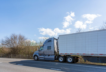 Gray big rig semi truck with refrigerated semi trailer standing of road on road shoulder