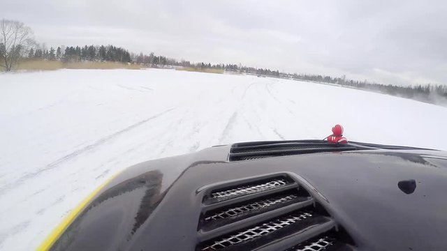 Car drives by icy track on snow covered lake at winter. Sport car racing on snow race track in winter. Driving a race car on a snowy road