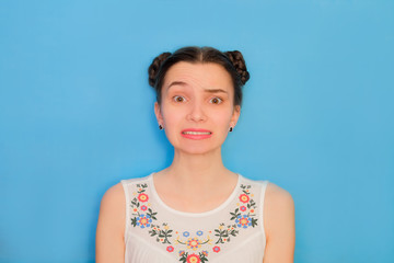 Funny cute girl on a blue studio background. Bright emotional female portrait. Failed grimace face