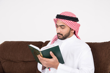 Arab Muslim man sitting on sofa chair and reading the holy Quran