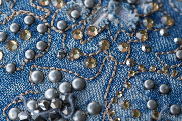 Blue denim fabric decorated with shiny and silver beads decor. Macro top view photography.