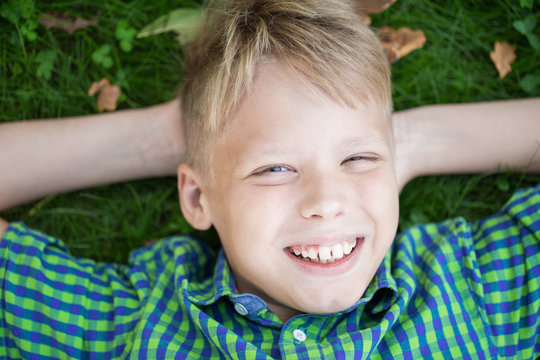 Close Up Top View Photography Of Cute Young Laughing White Kid Laying Down On Grass Outside. 