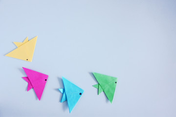 Four fishes of origami color paper on a blue background. Children's creativity. Art of paper. Copy...