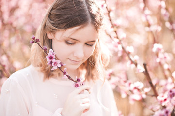 Smiling blonde girl holding peach flowers outdoors closeup. Spring season.
