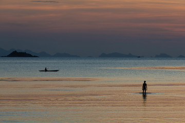 Fototapeta na wymiar Fisherman standing on a low tide at evening sky background in the sea water