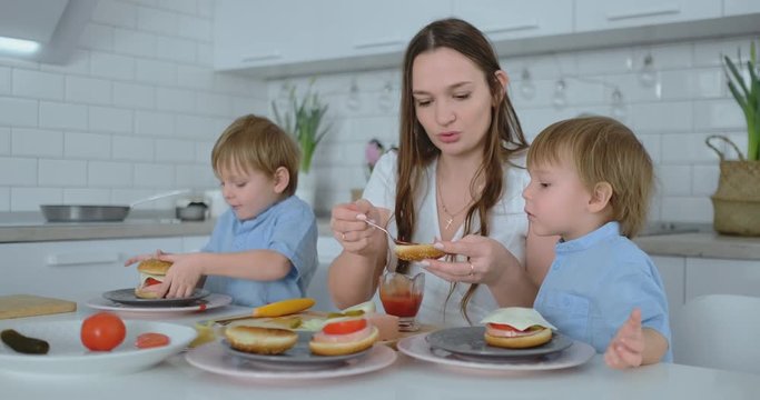 Beautiful young mother with two children sons on white light kuna cook with burgers
