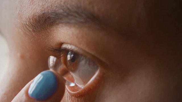 A beautiful young girl puts contact lenses in her eye close-up, macro. Blinking distributes the lens in the pupil. Brown eyes, black eyelashes, transparent lenses. Slow motion, 4K