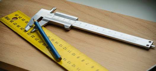caliper and pencil on wooden background