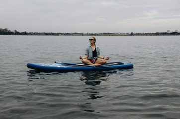 Young woman doing yoga on sup board with paddle. Meditative pose