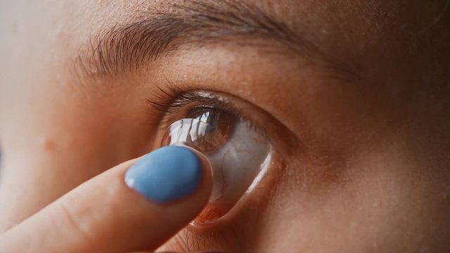A beautiful young girl puts contact lenses in her eye close-up, macro. Blinking distributes the lens in the pupil. Brown eyes, black eyelashes, transparent lenses. Slow motion, 4K