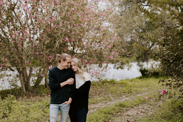 Young Couple in Love Holding One Another Outside in Nature in From of Cherry Blossom Tree and Pond