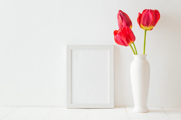 Mockup with a white frame and red tulips in a vase on a white wooden table