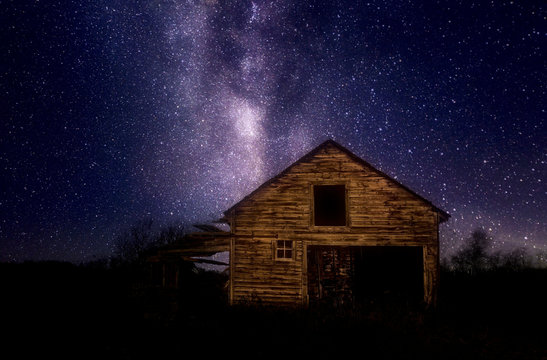 A crumbling wooden car garage under a star filled night sky in a rural landscape