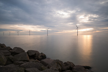 Windpark im Meer mit Steinküste im Sonnenuntergang