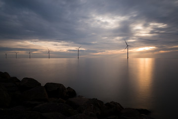 Windpark im Meer mit Steinküste im Sonnenuntergang dunkel