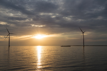 Binnenschiff und Windkraftanlage vor der Küste im Sonnenuntergang 