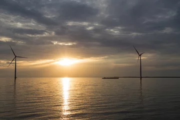 Deurstickers Binnenschiff und Windkraftanlage vor der Küste im Sonnenuntergang  © Marius Grobecker
