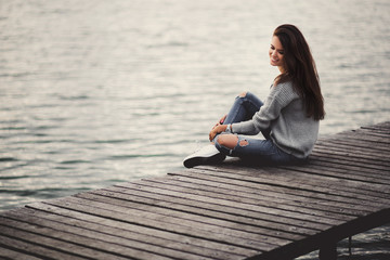 Beautiful dreaming woman sitting on pier by the lake.