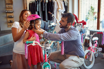 father and mother shopping new bicycle and helmets for little girl in bike shop .