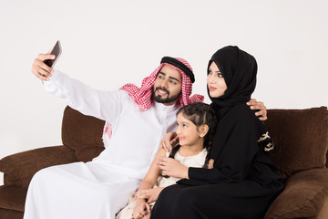 Arab family using smart phone and taking selfie while sitting on sofa chair at home