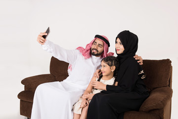 Arab family using smart phone and taking selfie while sitting on sofa chair at home