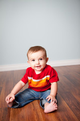 Naklejka premium Happy Baby Boy Sitting on Wood Floor in Home - Color Portrait