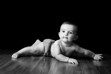 Fototapeta na wymiar Happy Baby Boy Lying on Wood Floor - Black and White Portrait