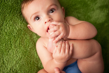 Teething Baby Boy Chewing on His Toes While Lying on Green Carpet