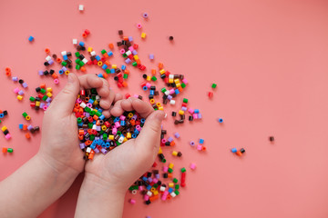 colorful beads on a pink background in children's hands