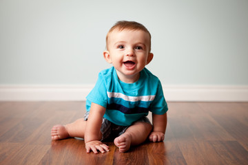 Happy Baby Boy Sitting on Wood Floor in Home