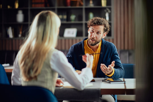 Two young attractive colleagues sitting in cafetaria and talking about project.