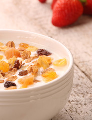 Bowl of yogurt with strawberries and granola muesli, over a white wood background.