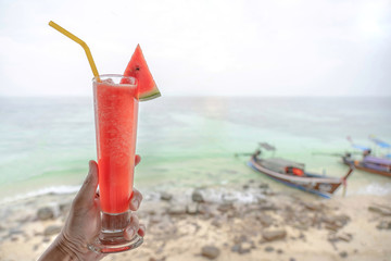 Hands holding glass of watermelon shake with long tail boat floating on the ocean.Happy enjoying in summer holiday.Tropical paradise at the island.Travel,Vacation,Nature,Day off Concept.