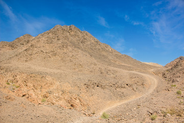 dry mountain in rocky desert outdoor wilderness natural environment scenic landscape with small trail for hiking and climbing, sand stones ground and vivid blue sky background