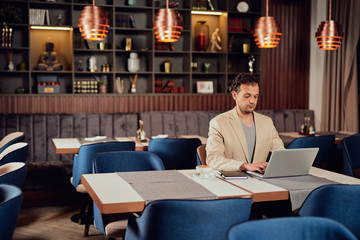 Attractive arab businessman dressed smart casual sitting at cafe and using laptop.