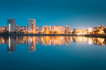 Fototapeta na wymiar Night View Of Urban Residential Area Overlooks To City Lake Or River And Park In Evening Illumination, Reflecting In Water Surface.