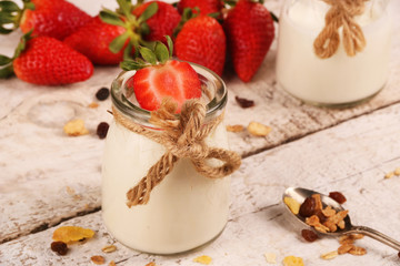Jar with delicious yogurt and strawberry and granola muesli, over a white on wooden table
