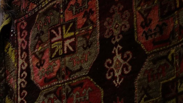 Steady, close up, interior shot of a hanging rug containing patterns and symbols. Rack focus to blur out rug.