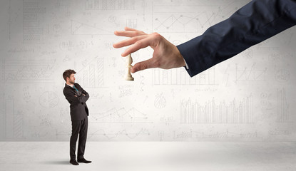 Little businessman is afraid to make the next step in his chess game with graphs, charts and...