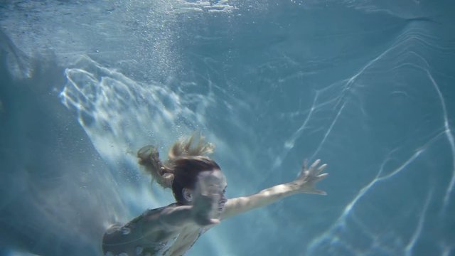 Young blonde woman in vintage white dress swim underwater