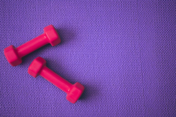 Top view of purple yoga mat with bright pink dumbbells with copy space 