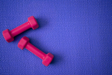 Top view of blue yoga mat with bright pink dumbbells with copy space 