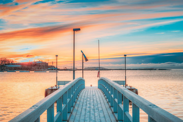 Obraz premium Old Frosted Wooden Boards Pier On Calm Water Of Lake Or River Or Sea At Evening Or Morning Time. Sunset Sunrise In Winter Season