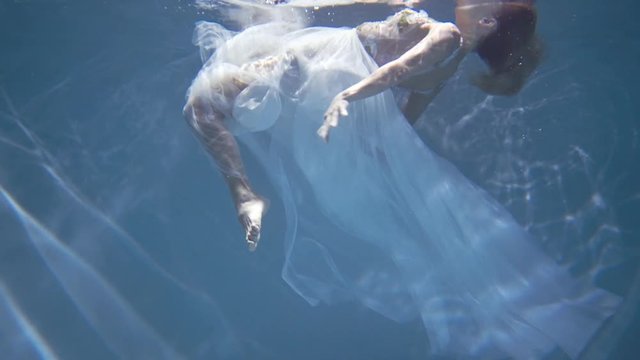 Young blonde woman in vintage white dress swim underwater