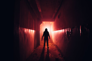 Creepy silhouette with knife in the dark red illuminated abandoned building. Horror about maniac...