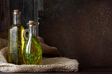 Olive oil with herbs in transparent bottles on a dark background. Rustic. Copy space.
