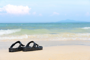 Sandal flip flop on the sand beach with blue ocean sea and sky background in summer...
