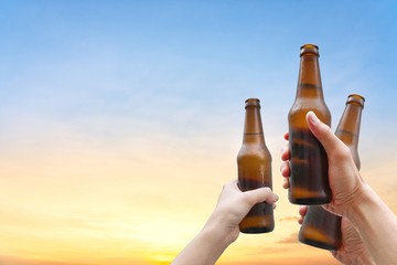 Hands holding three beer bottles and happy enjoying harvest time together to clinking glasses at outdoor party on beautiful sunset background.Celebration drinking beer.       